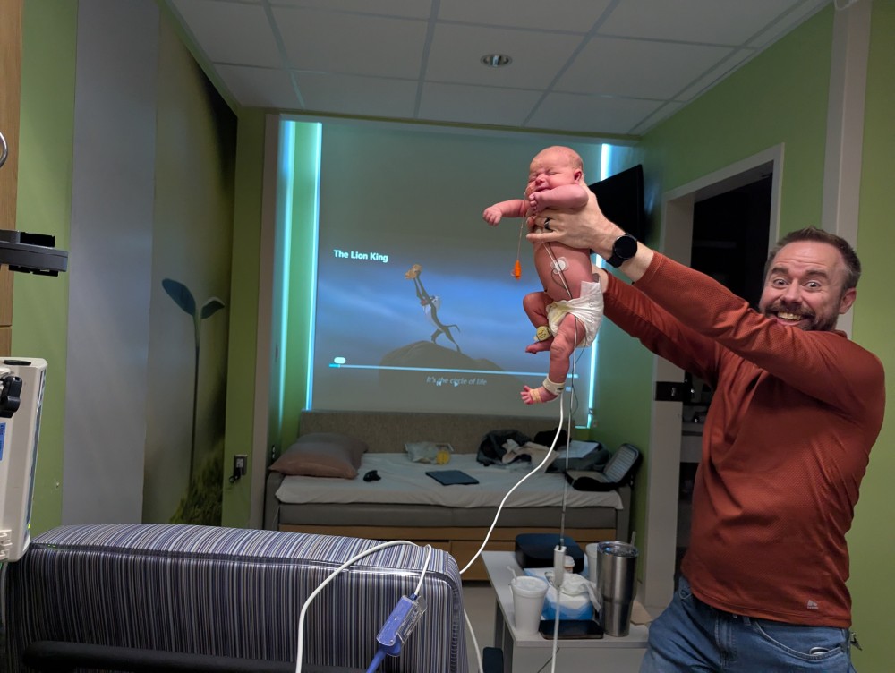 Shane Reichart holds baby Vienna in the Lion King pose in front of a projected Lion King movie