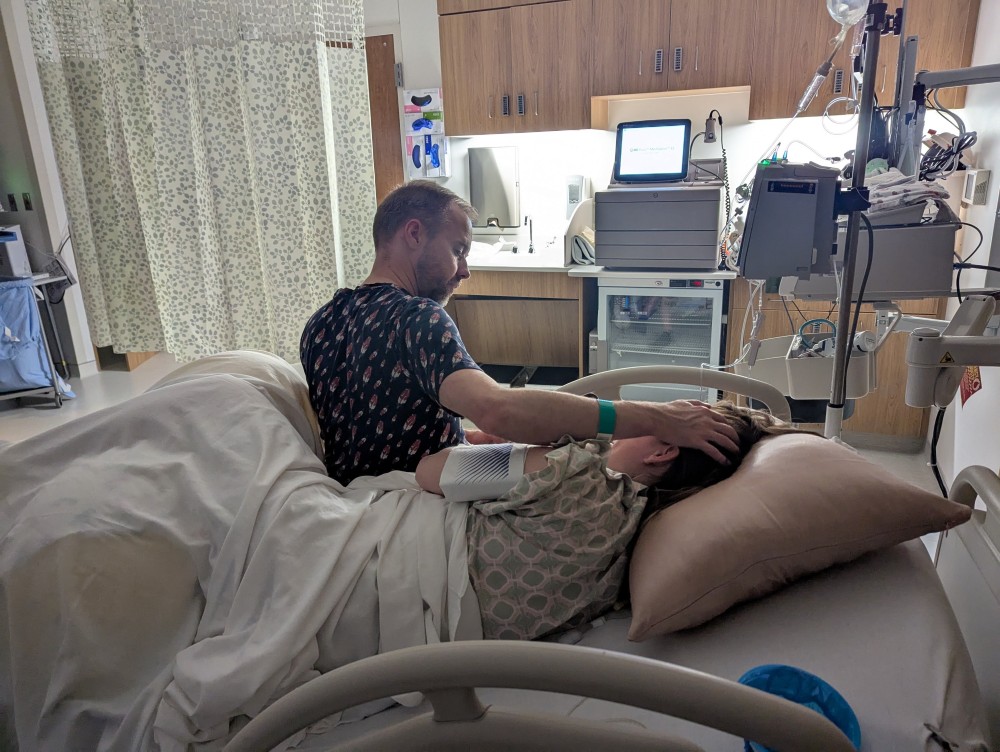 a man, Shane Reichart, praying over a woman, Amanda Reichart, in the delivery room
